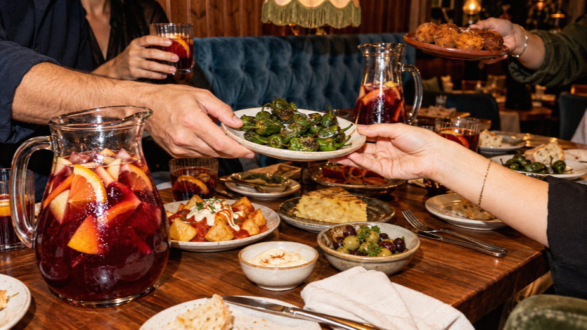 Friends passing plates of tapas and a jug of sangria across a busy table